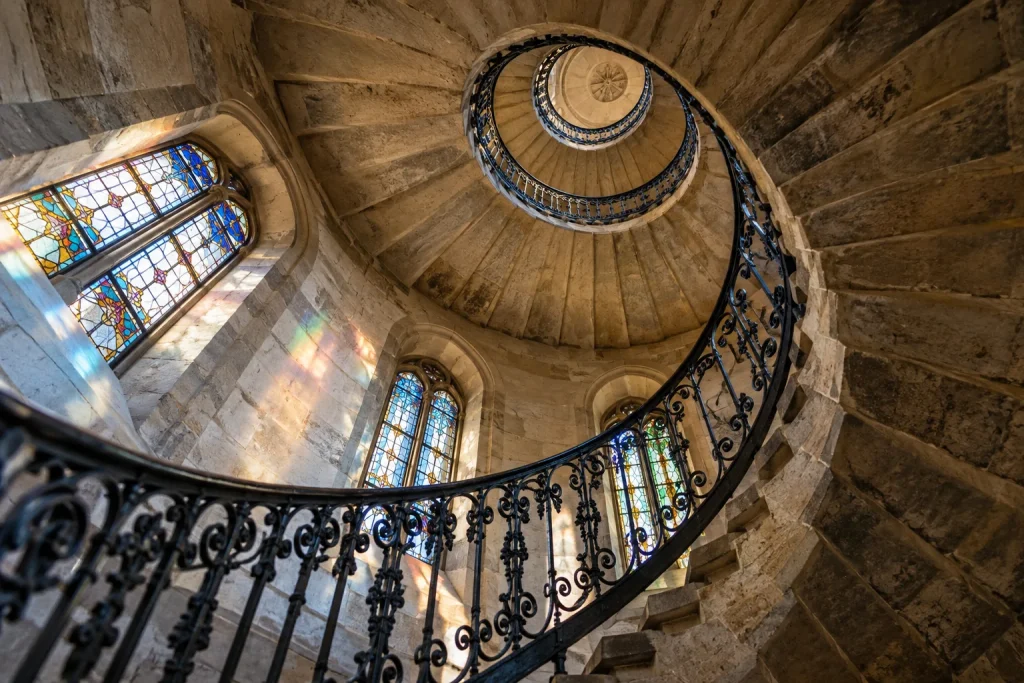 Symbolmotiv: Blick durch eine historische Wendeltreppe mit farbigen Lichtreflexen.