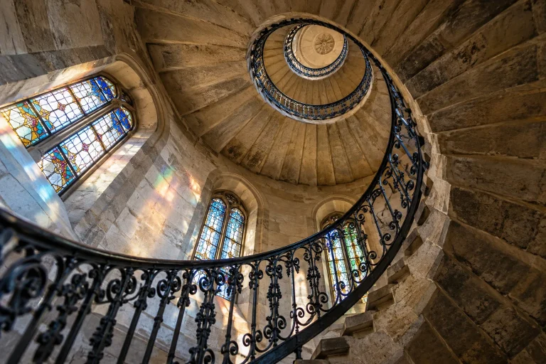 Symbolmotiv: Blick durch eine historische Wendeltreppe mit farbigen Lichtreflexen.